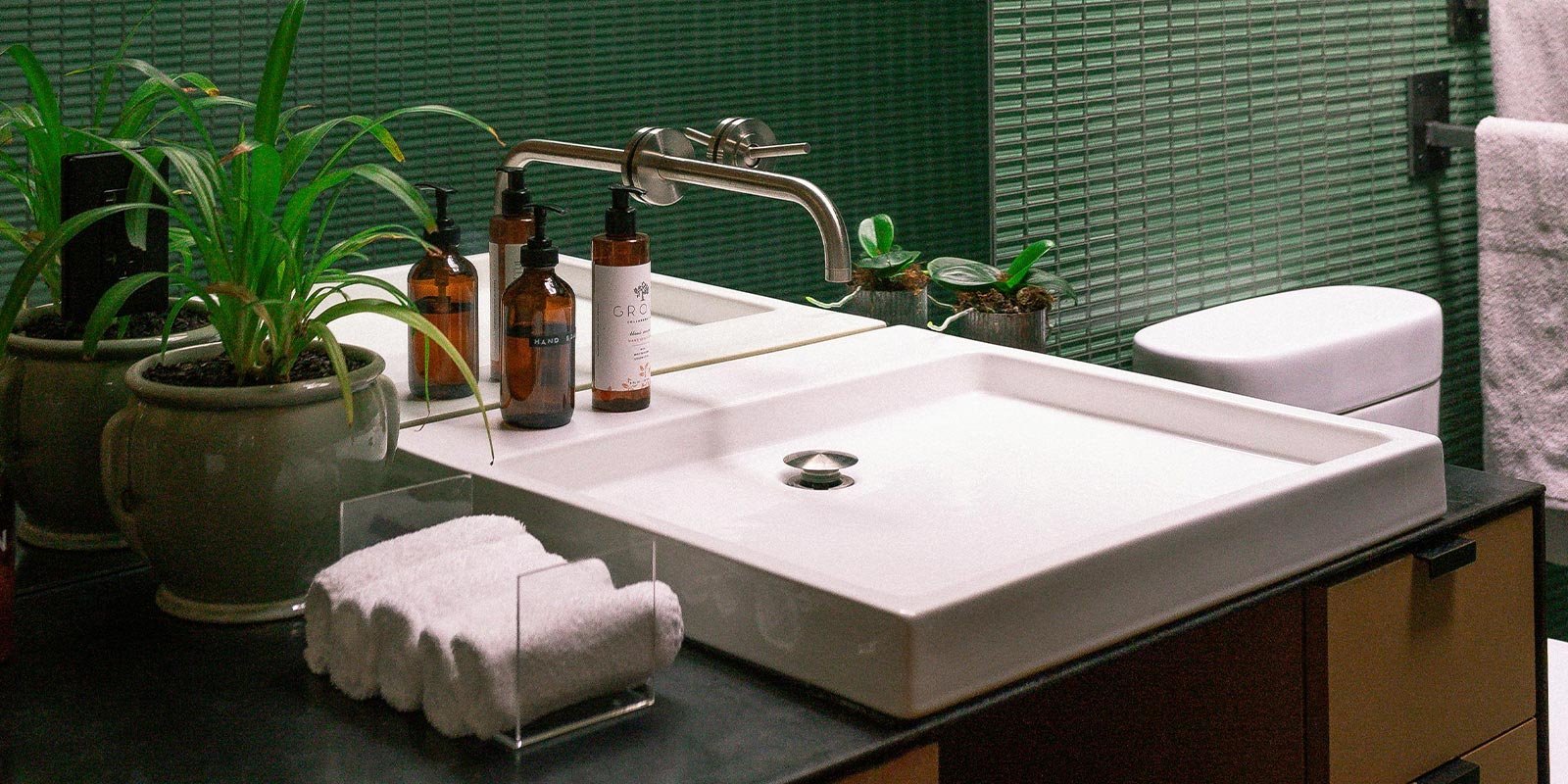 Ein modernes Badezimmer mit einem eleganten Waschbecken, umgeben von Pflanzen und stilvollen Pflegeprodukten auf dem Tisch.