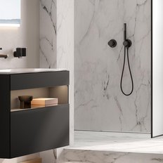 Ein modernes Badezimmer mit einem eleganten schwarzen Waschbecken und einem großen Spiegel, der sanft beleuchtet ist.