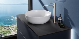 Ein elegantes Waschbecken aus weißem Keramik steht auf einem modernen schwarzen Tisch, mit Blick auf das ruhige Wasser draußen.