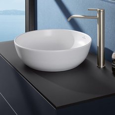 Ein elegantes Waschbecken aus weißem Keramik steht auf einem modernen schwarzen Tisch, mit Blick auf das ruhige Wasser draußen.